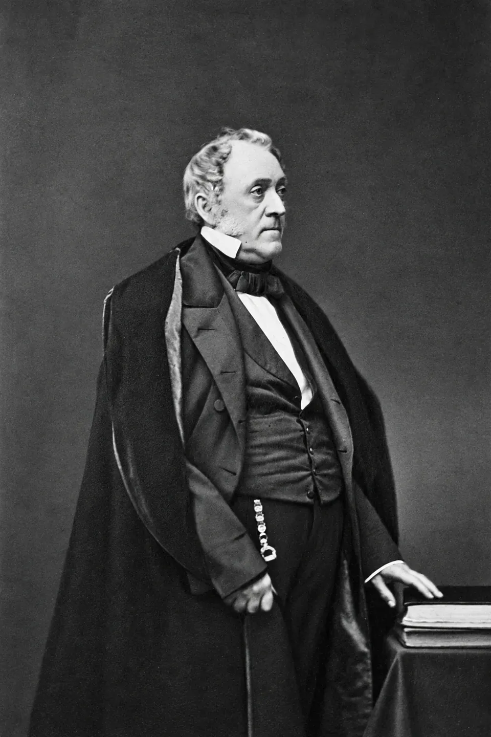 Valentine Mott stands in a dark coat beside a table and books in a nineteenth-century studio portrait.