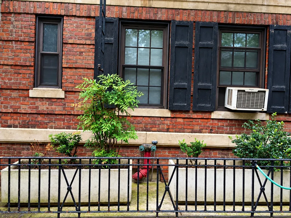 Brickwork, shuttered windows, planters, and an iron fence at street level.