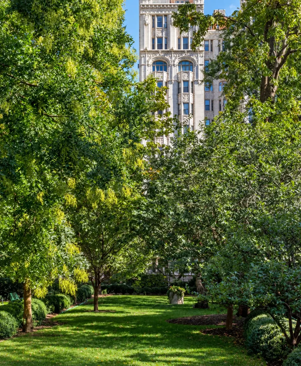 The pale facade of 36 Gramercy Park East seen through trees above a lawn inside Gramercy Park.