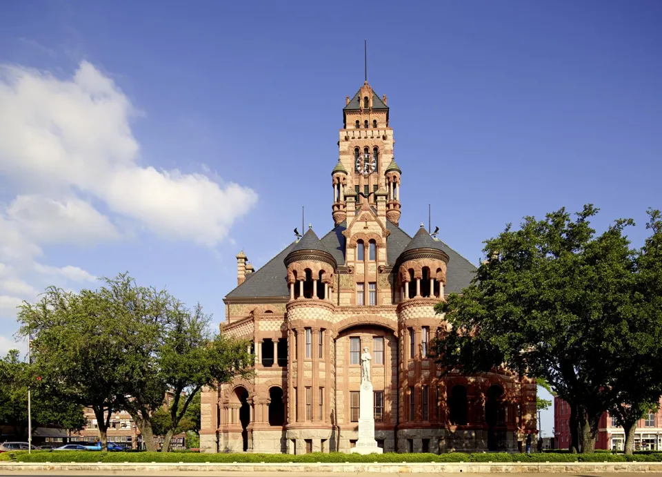 The red sandstone Ellis County Courthouse in Waxahachie, Texas, with arched windows and a tall central clock tower.