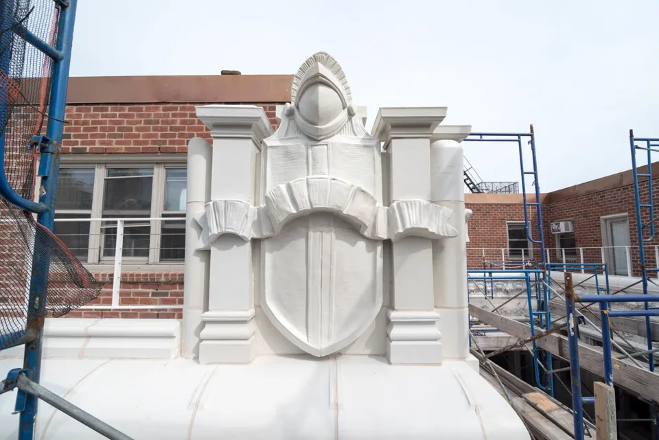A helmeted figure and shield at the roofline, beside scaffolding during restoration.