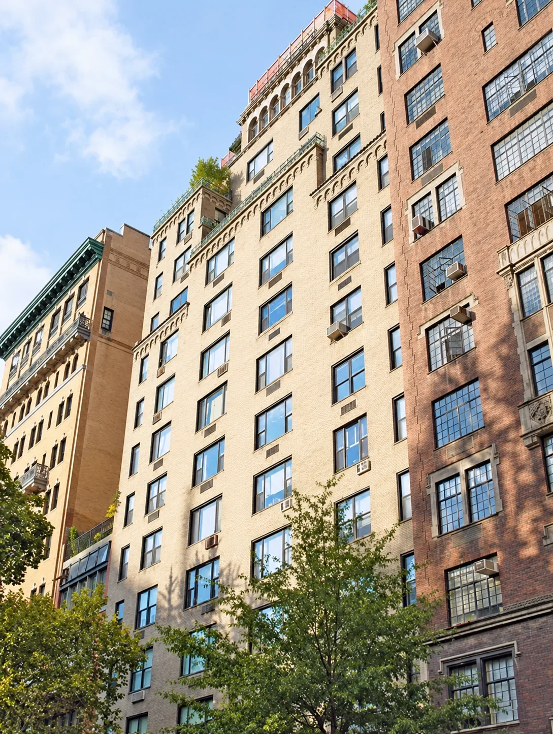 The buff-brick and limestone facade of 45 Gramercy Park North rising above the trees on the north side of Gramercy Park.