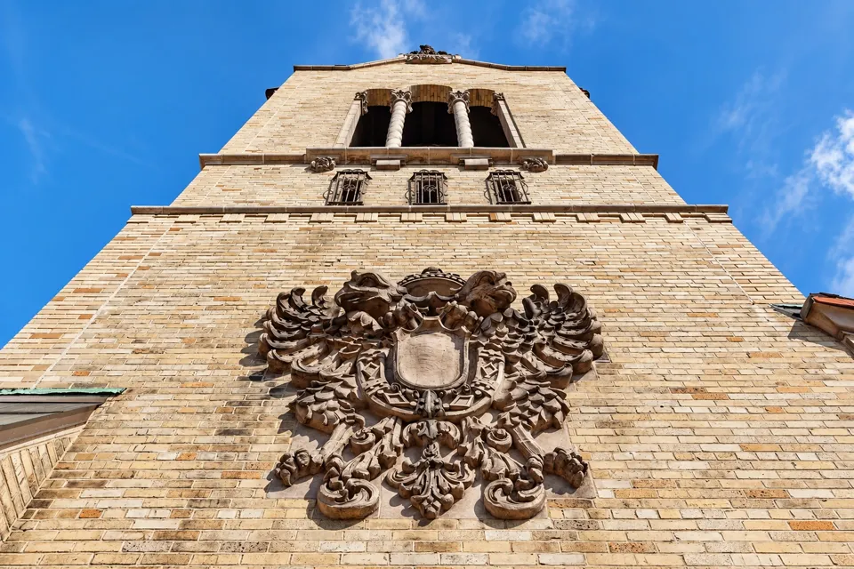 A terra-cotta cartouche below the tall triple arches of the rooftop tower.