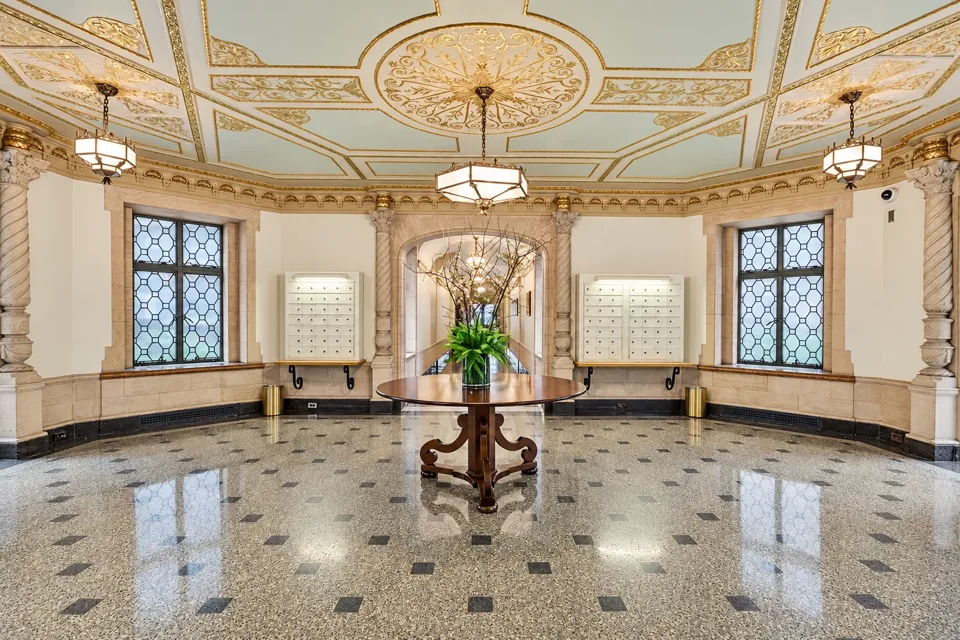 A wide view of the circular lobby, with gilded ceiling panels, leaded-glass windows, mailboxes and a central flower table.
