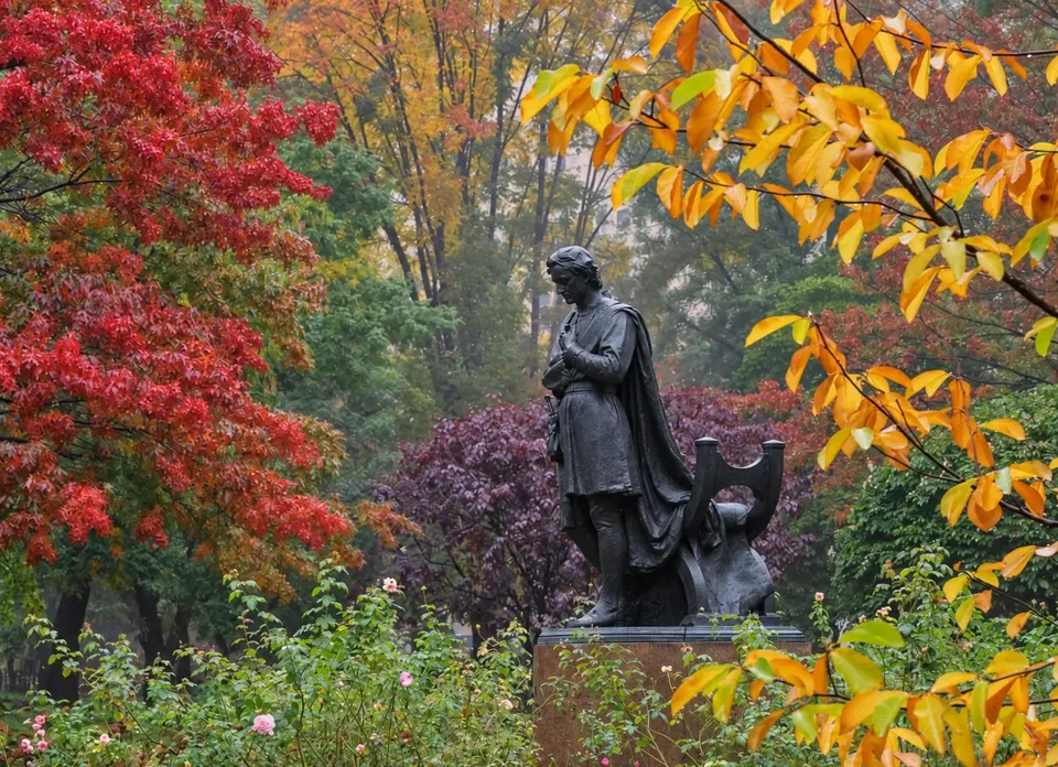 The Booth statue viewed through yellow and red autumn foliage in Gramercy Park.