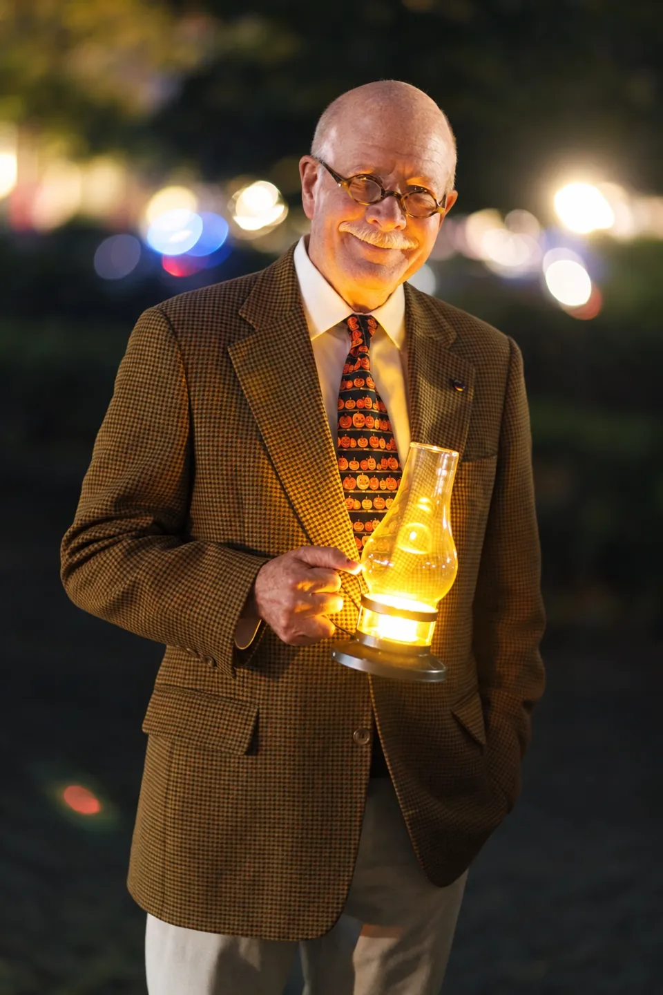 A participant in a checked jacket and glasses holds a glowing lantern at the Booth birthday gathering.