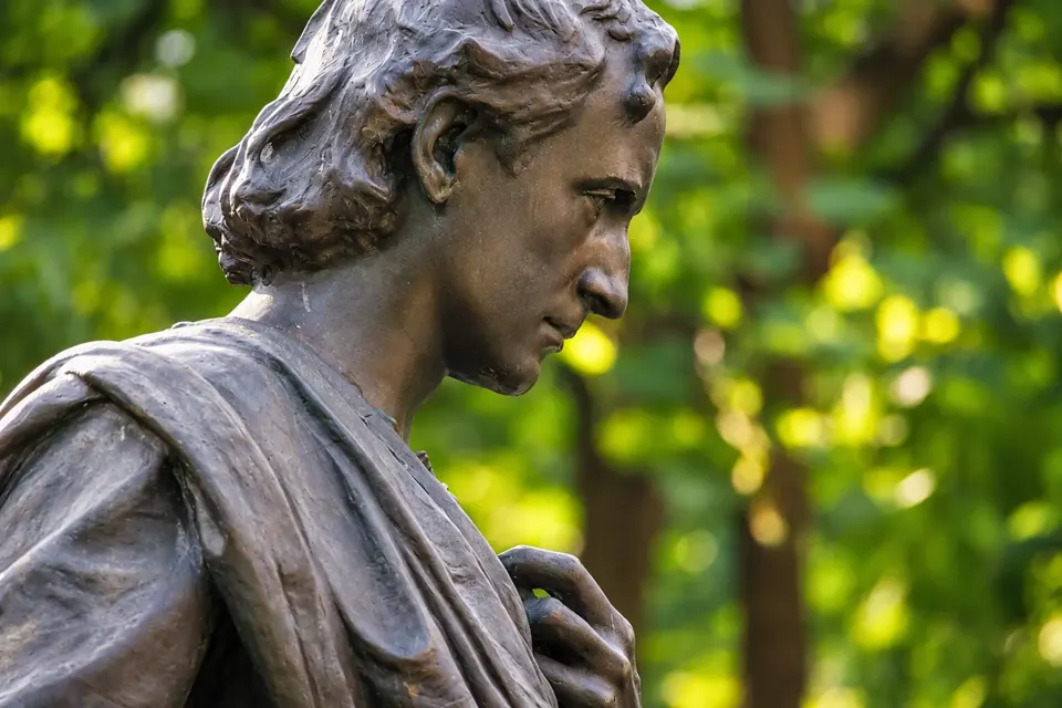 Close view of the bronze statue’s bowed head, wavy hair, tunic and cloak.