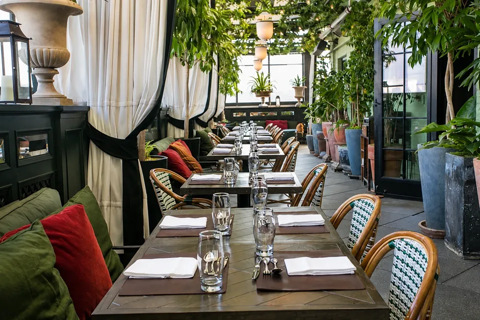 Set dining tables, wicker chairs, green plants, and lanterns along Gramercy Terrace.