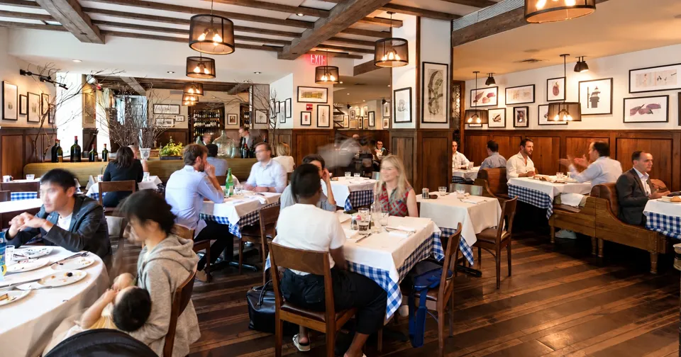 Diners at Maialino, with white tablecloths, checked table skirts, and wood-paneled walls.