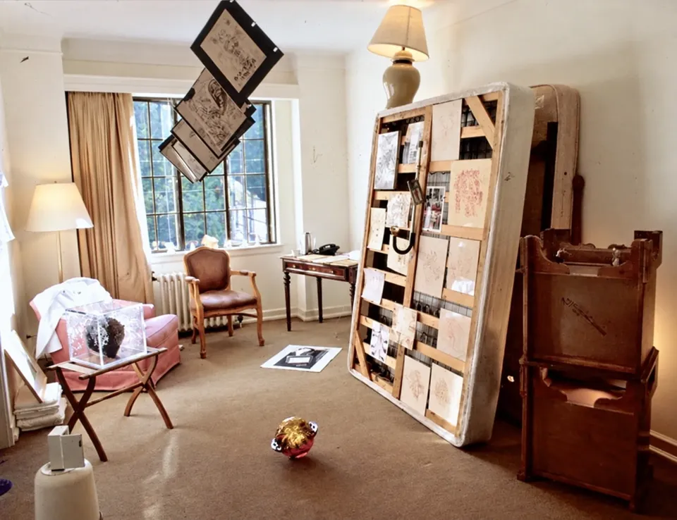 An installation by Rachel Harrison in a hotel room, with artworks attached to an upright mattress and suspended from the ceiling.