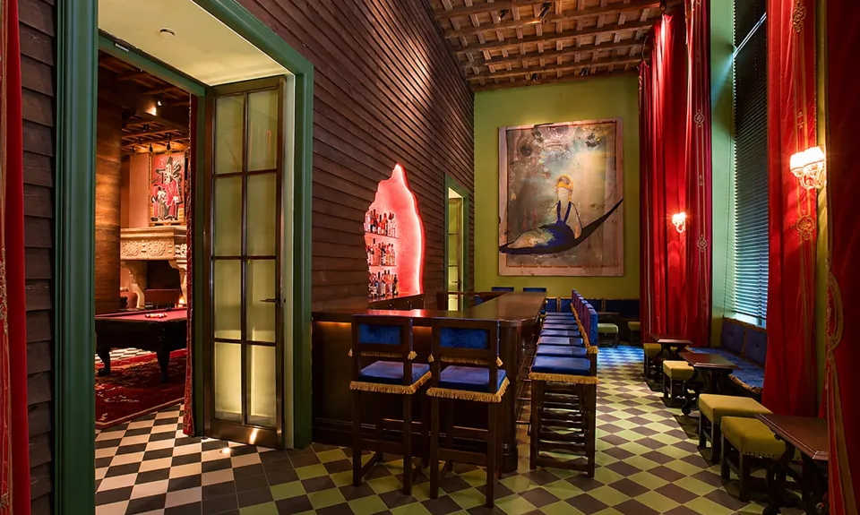 Green walls, red curtains, blue bar stools, paintings, and a checkerboard floor in the redesigned hotel.