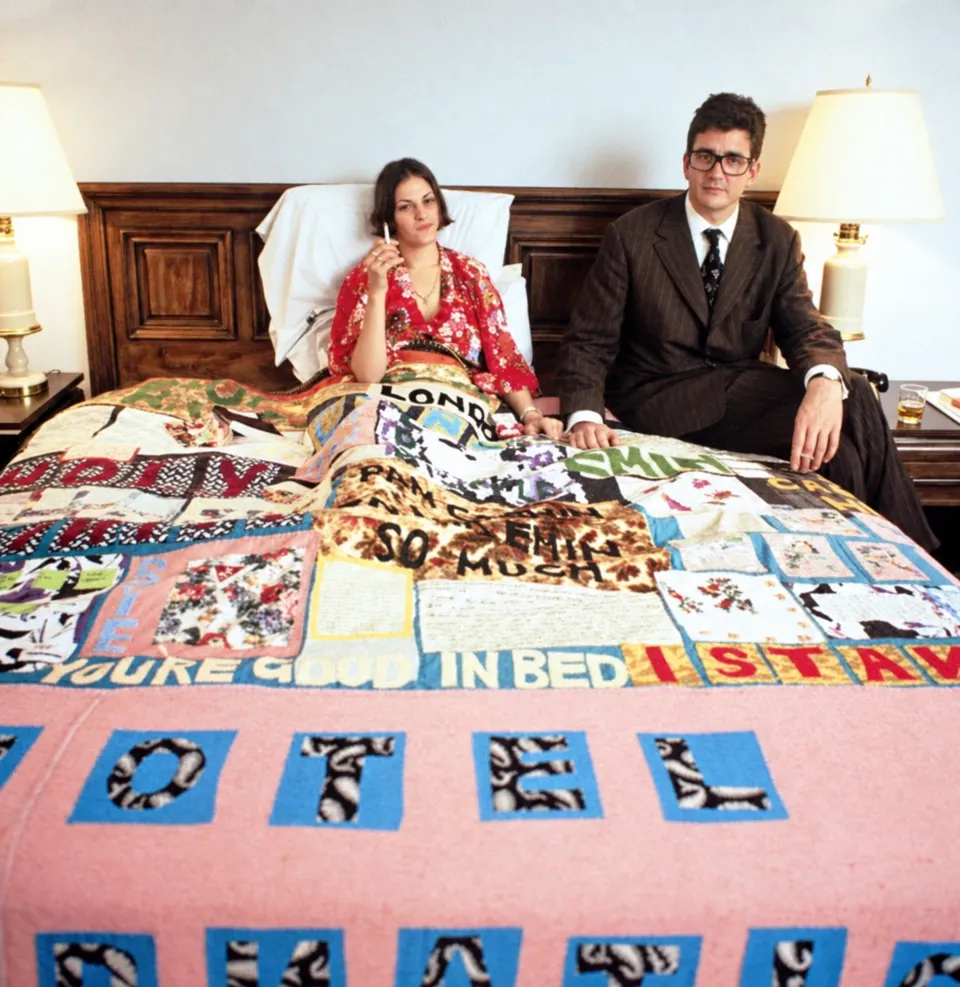 Tracey Emin and Jay Jopling seated on a hotel bed covered with Emin’s appliquéd blanket Hotel International.