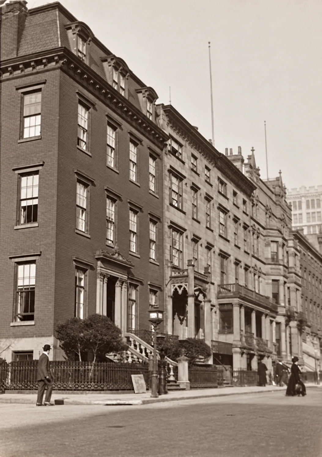 Historic view west along Gramercy Park South, with houses, apartment buildings, and people in the street.