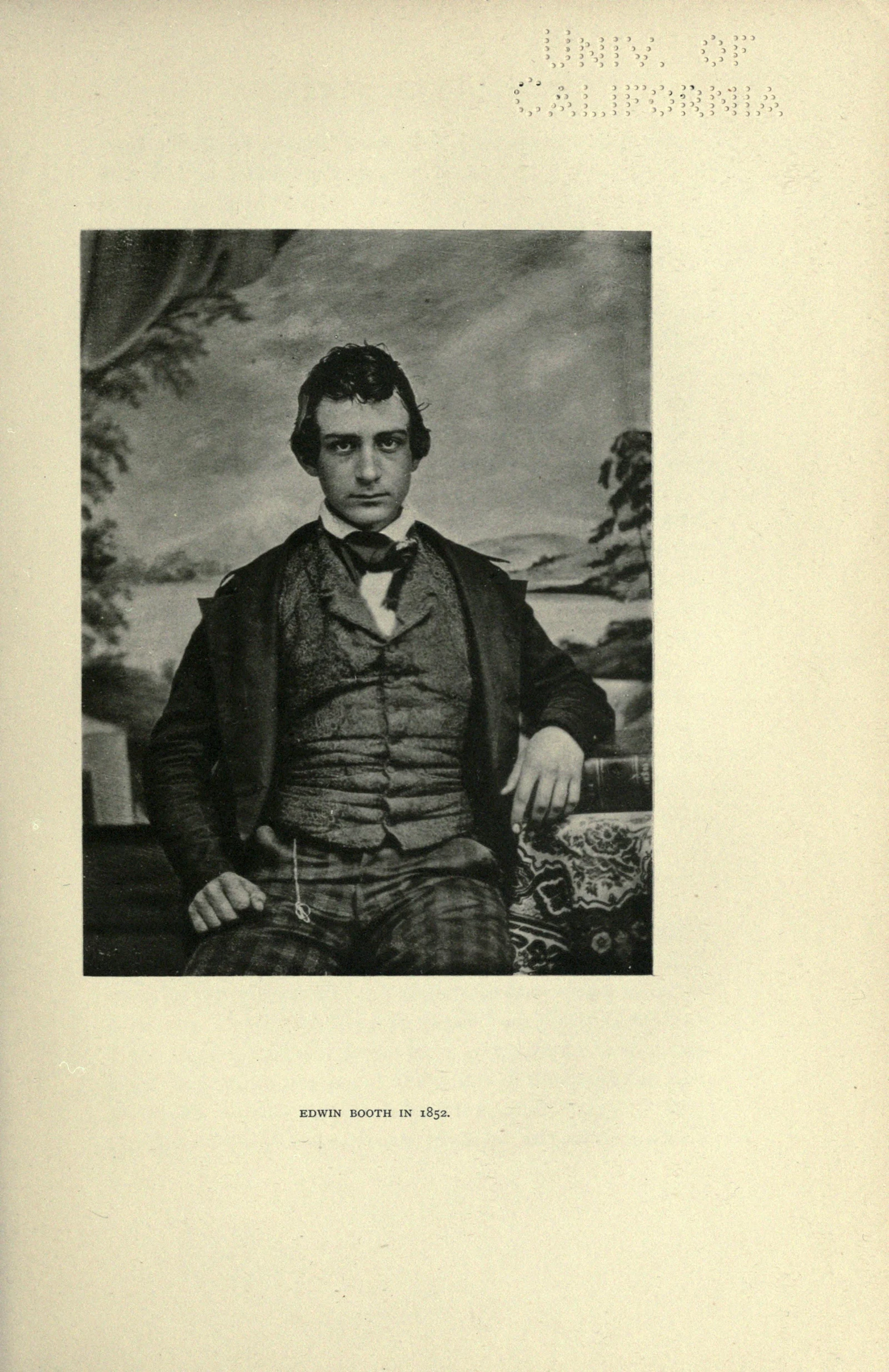 Young Edwin Booth faces the camera in a waistcoat and bow tie, one hand on a chair.