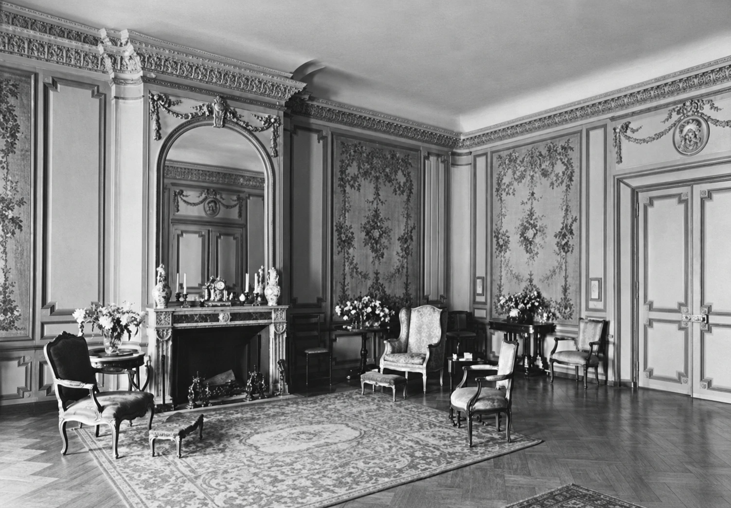 Chairs, flowers, a patterned carpet, and a tall mirror above the fireplace in the Barlows’ living room in 1931.