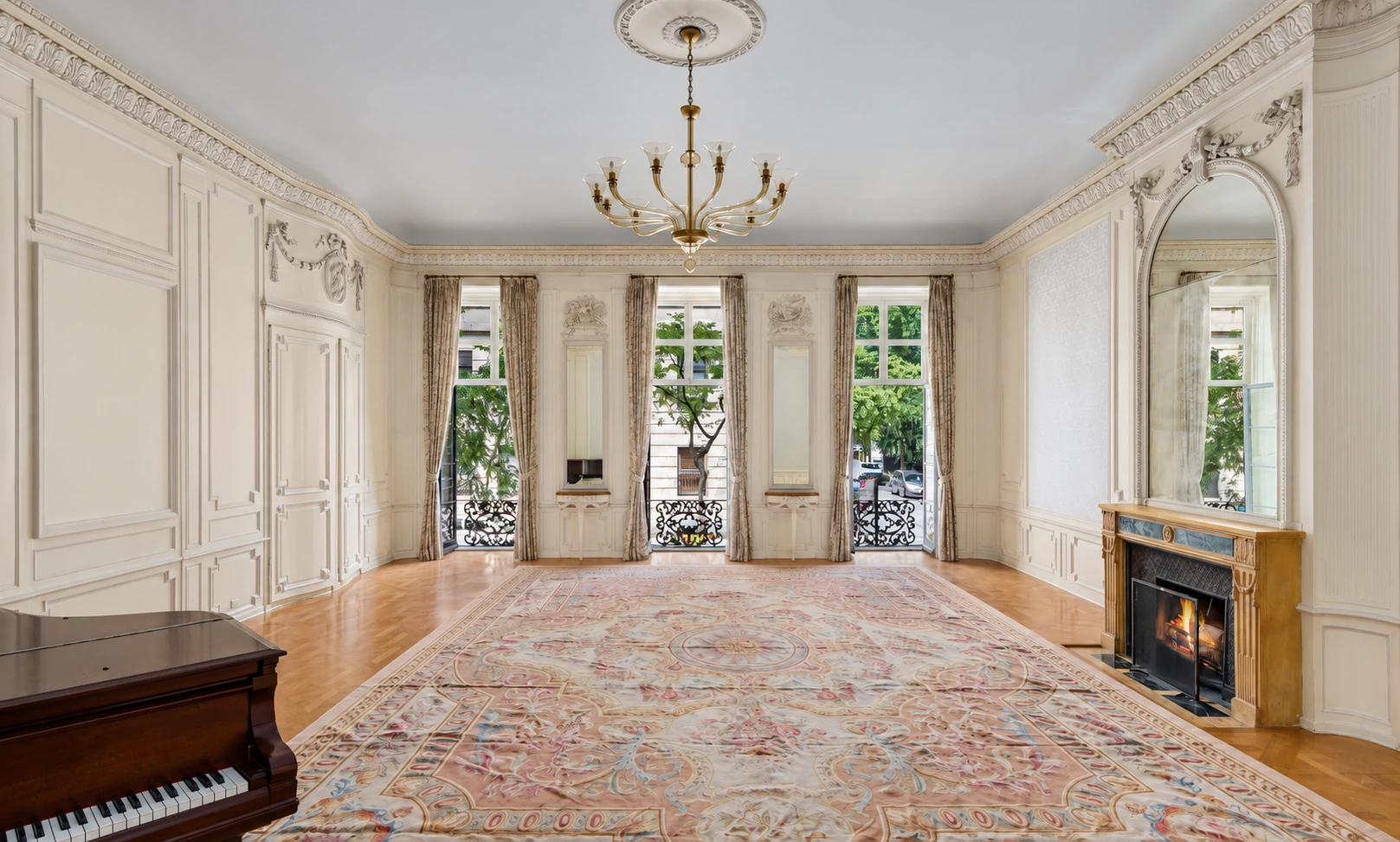 The Park-facing music room at 11 Gramercy Park South, with three tall windows, decorative wall panels, a fireplace, and a piano.