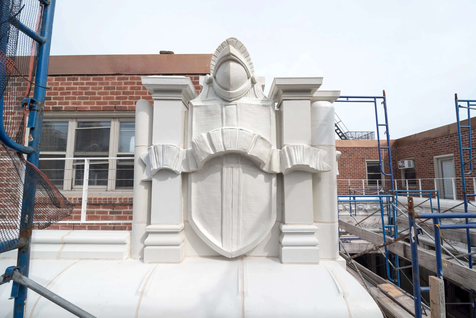 A helmeted figure and shield at the roofline, beside scaffolding during restoration.