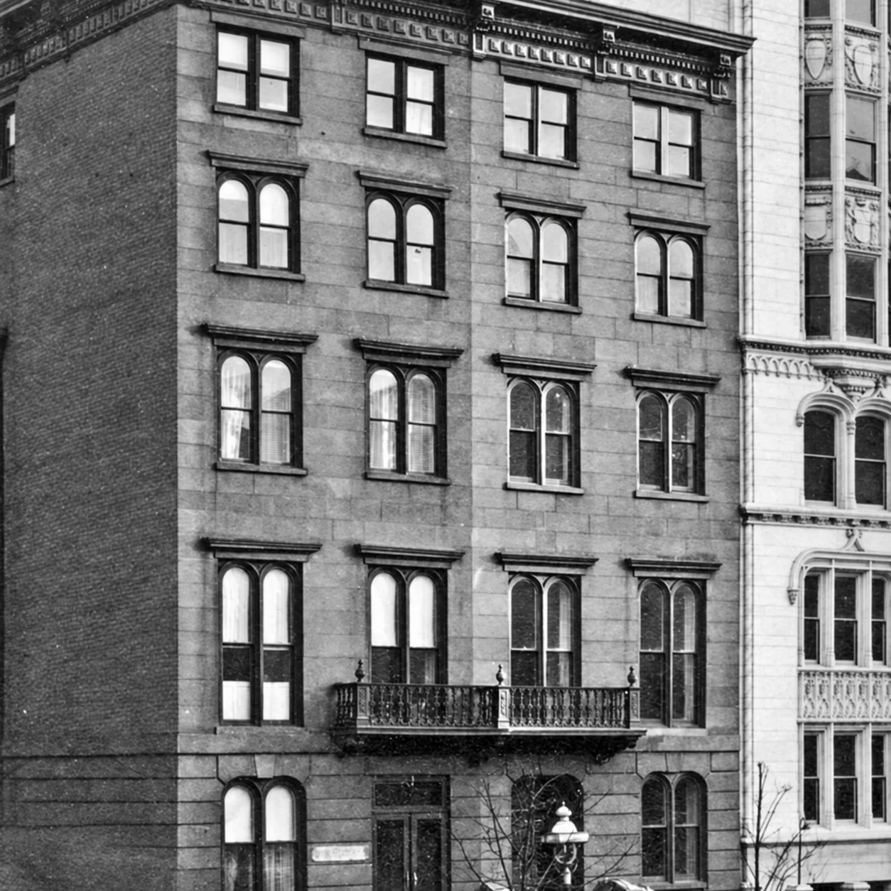 Black-and-white archival view of the earlier brownstone elevation, paired round-arched windows, balconies, and cornice.