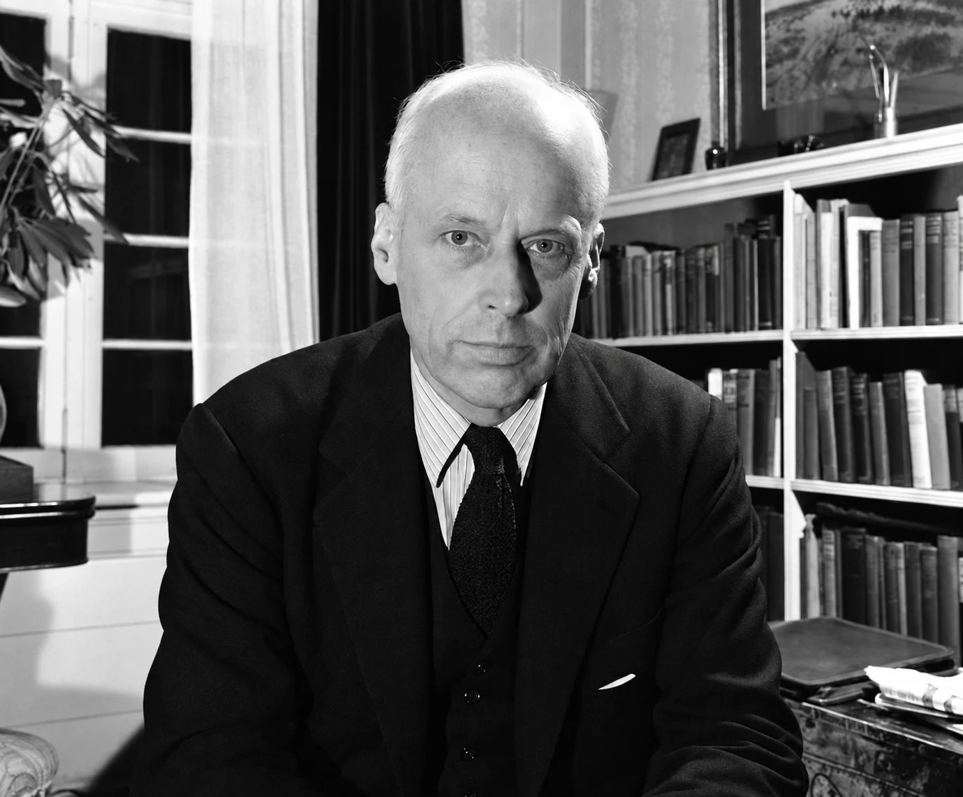 Norman Thomas seated beside bookshelves in an archival black-and-white portrait.