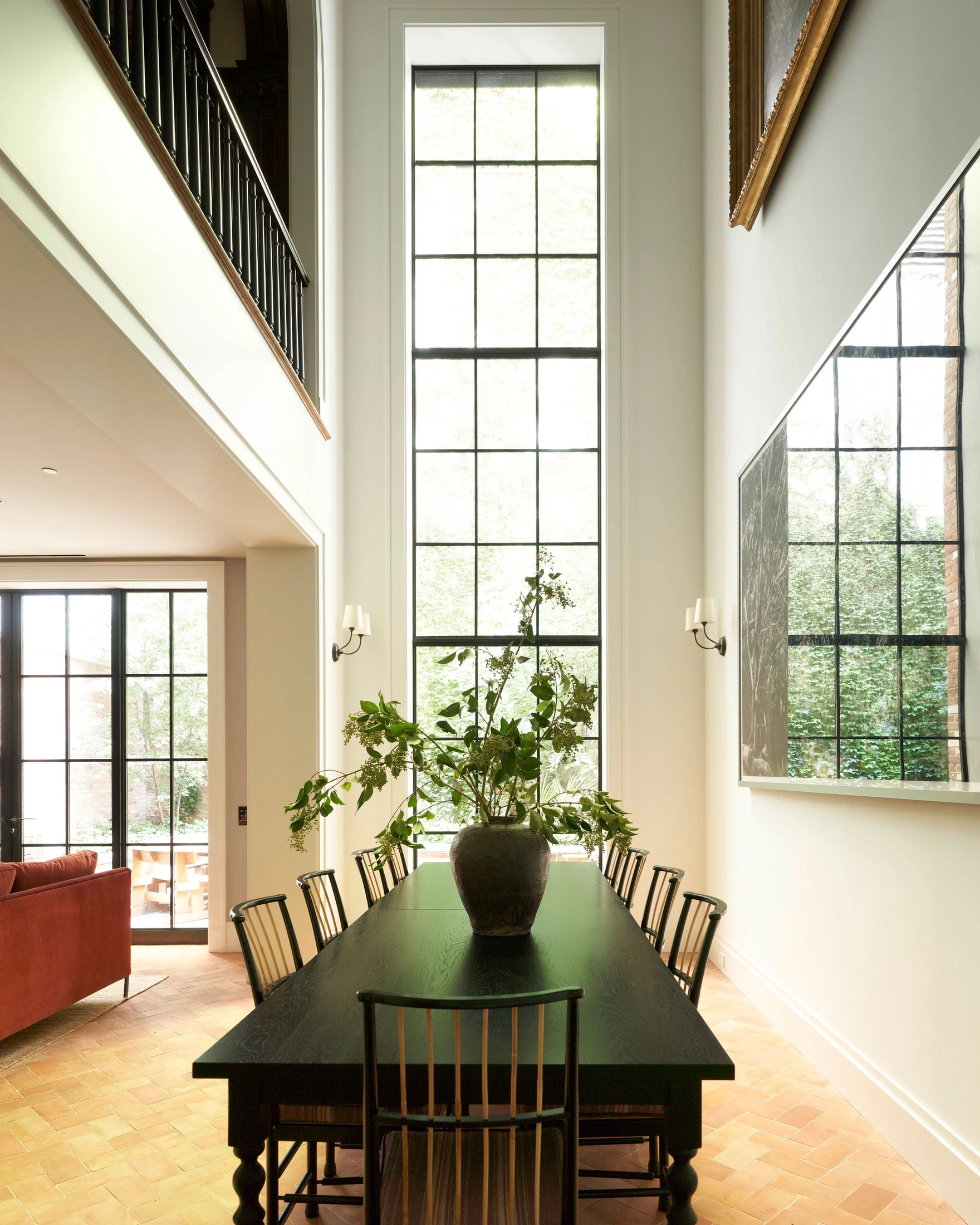 A double-height dining space beside a tall window facing the rear garden, with an opening to the salon above.