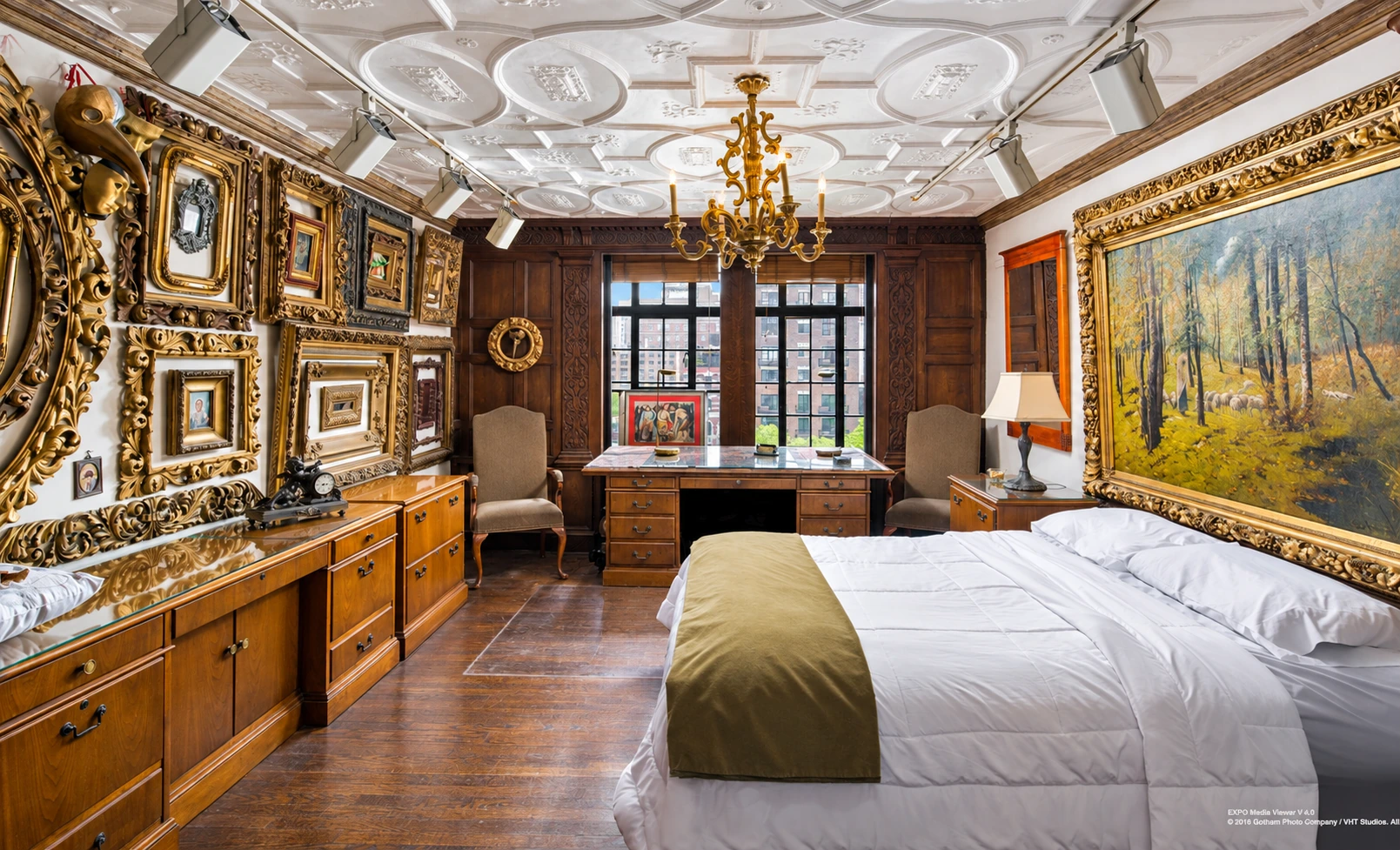 A bedroom with an ornate plaster ceiling, paneling and walls hung with gilded picture frames.