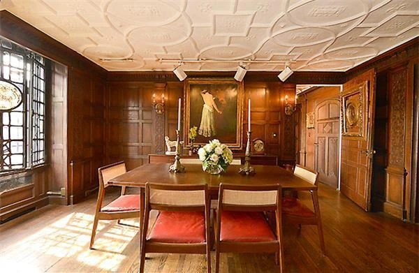 A paneled dining room with a long wooden table, red upholstered chairs and a decorated plaster ceiling.
