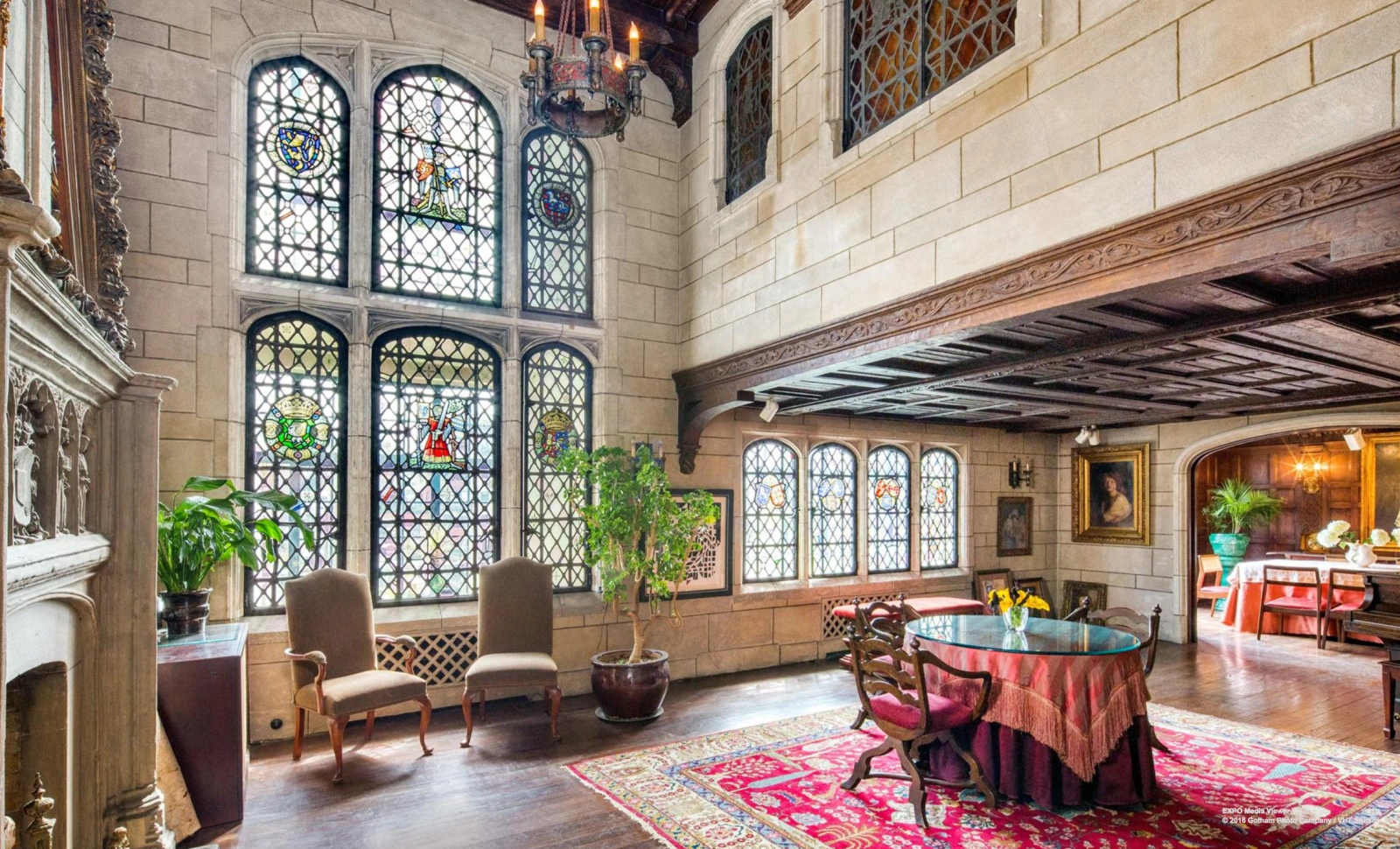 The double-height great room of the Aranyi–Llorente apartment, with stained glass, a timber gallery and richly colored furnishings.