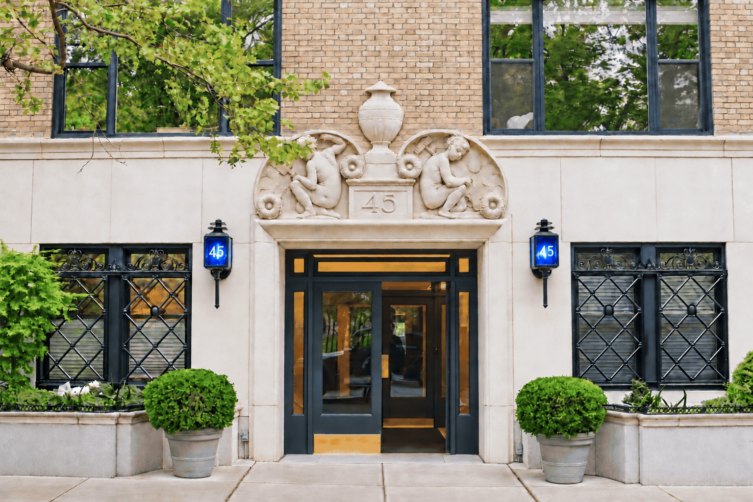 The limestone entrance of 45 Gramercy Park North, with two lanterns and carved figures flanking an urn above the doorway.
