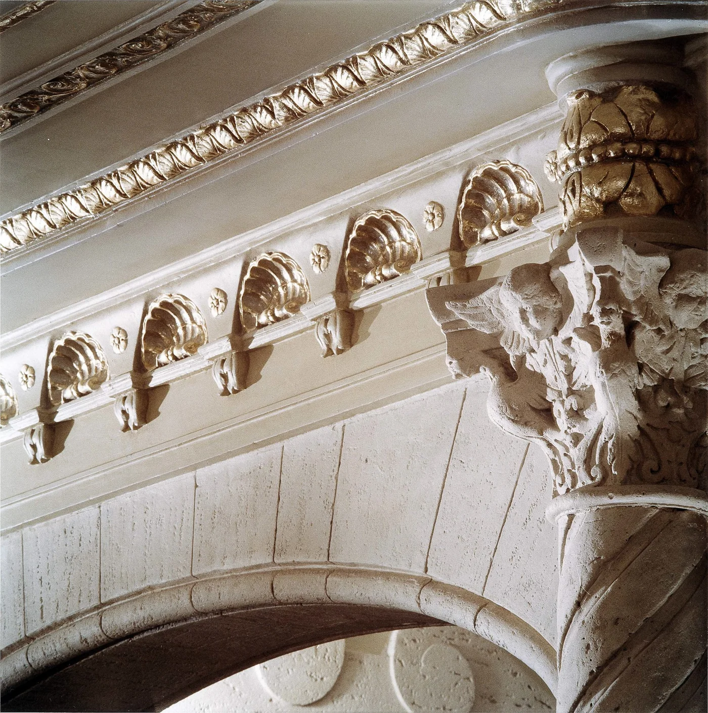 Gilded shells and a sculptural capital above a plaster arch in the lobby.
