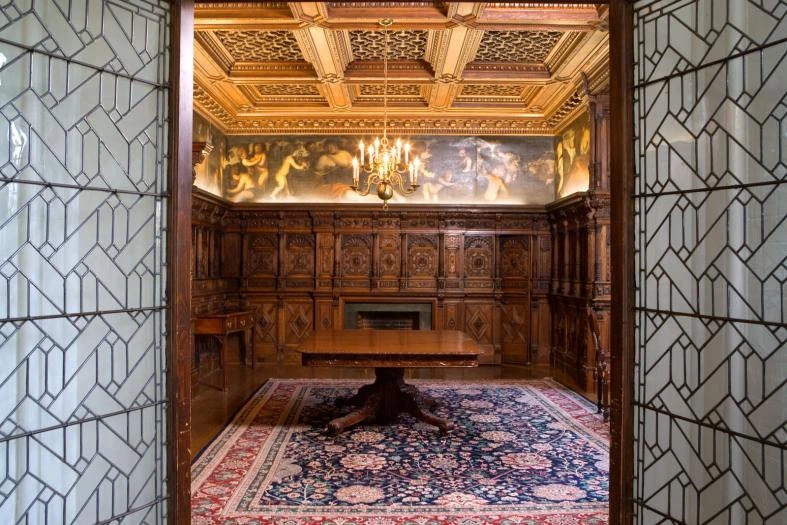 The former Cooper–Hewitt dining room reconstructed at Cornell, showing carved oak paneling, a painted mural and decorated ceiling
