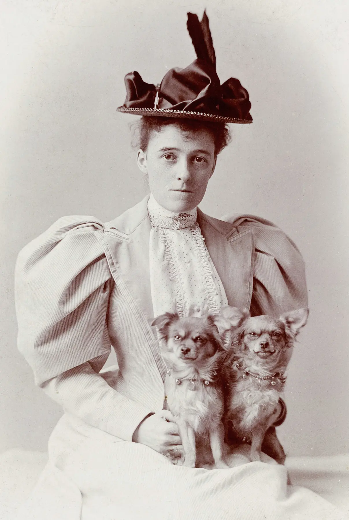 Edith Wharton seated outdoors in a long dress with two dogs beside her.