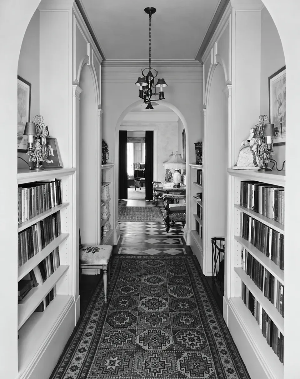 A hallway in Donald F. Crane’s apartment at One Lexington Avenue, lined with bookcases and patterned rugs beneath a hanging lantern, circa 1915–1930.