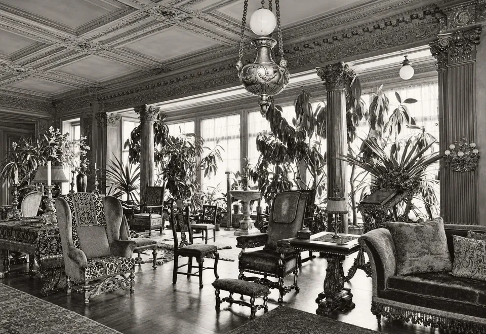 The conservatory in Henry W. Poor’s house, with glazed walls, plants and upholstered seating.
