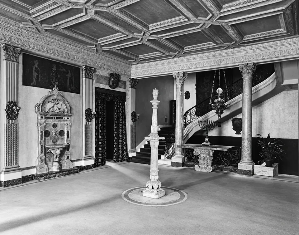 The hall in Henry Poor’s residence at One Lexington Avenue, with a carved ceiling, marble columns, wall fountain and sweeping staircase.