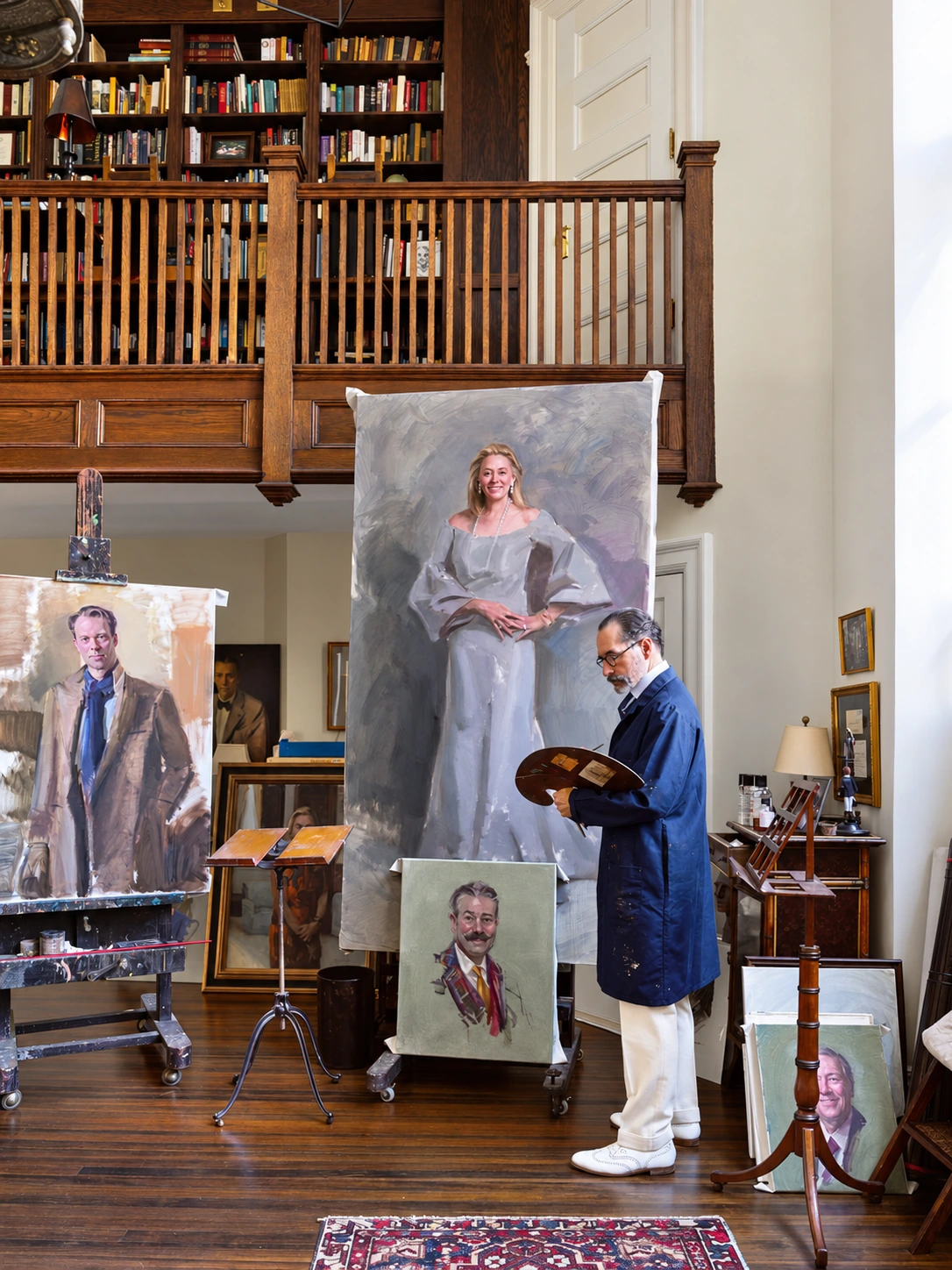 Michael Shane Neal with portraits and painting materials beneath the book-lined balcony in his National Arts Club studio.