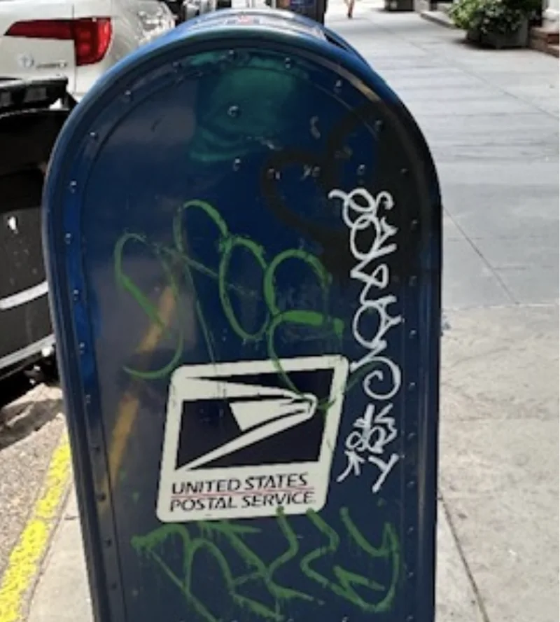 Green and white graffiti on a blue USPS collection box.
