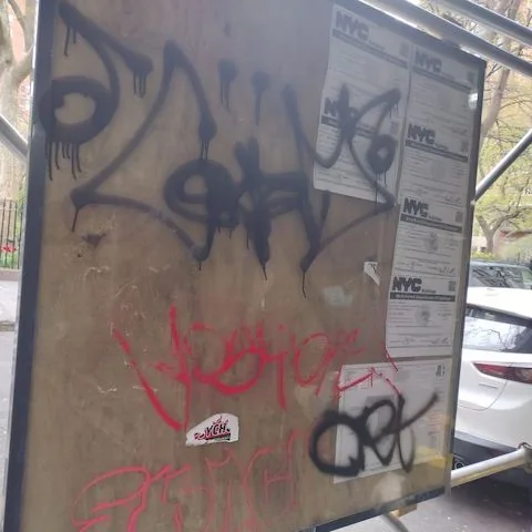 Graffiti on plywood beside construction notices.