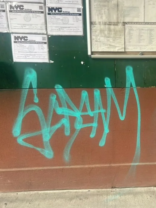 Teal graffiti on a two-tone construction wall beneath posted notices.