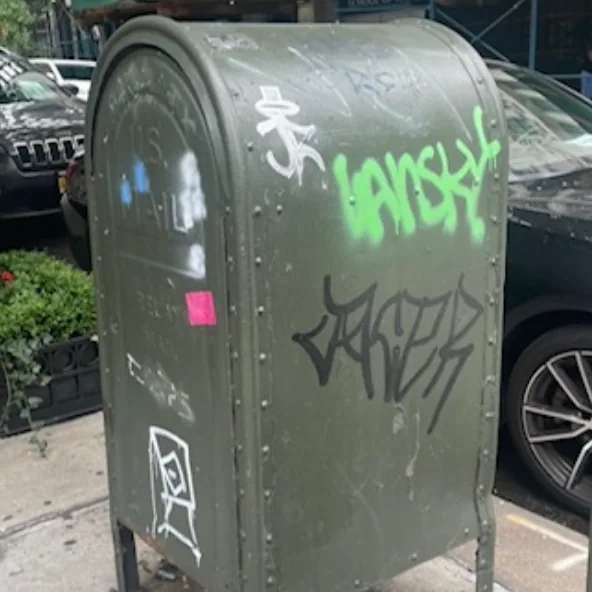 White, green, and black graffiti on a green mail relay box.