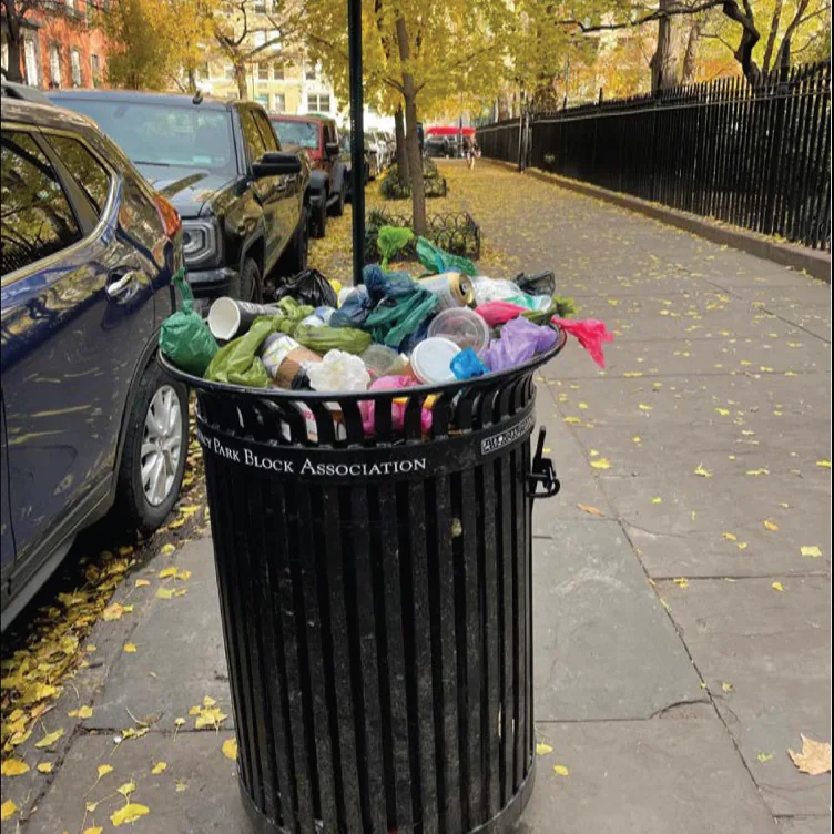 Cups and bags overflow from a litter basket along the Park fence.