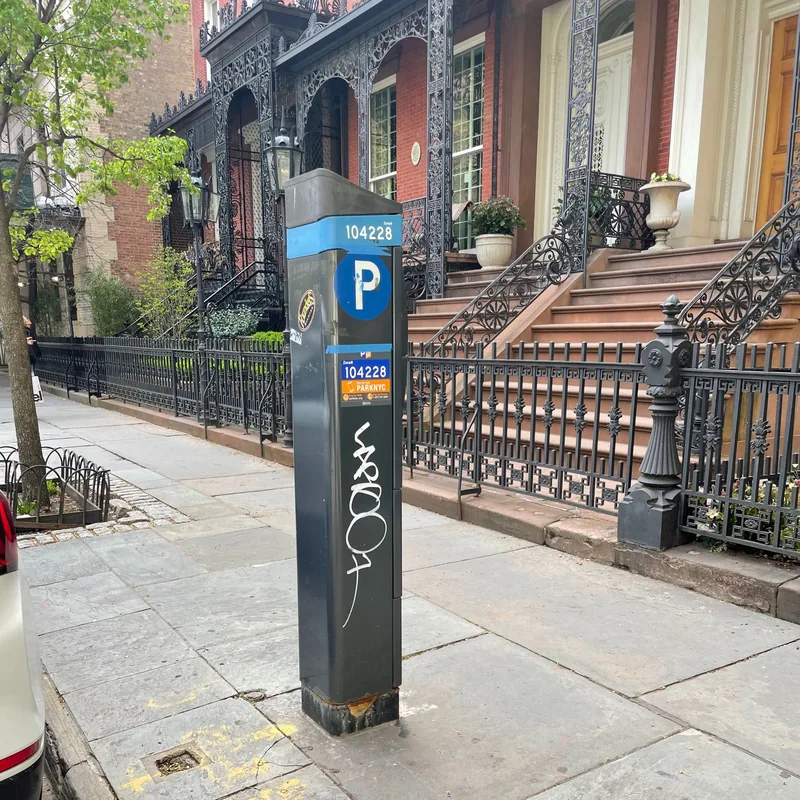 White graffiti on parking meter 104228 in front of brownstones.