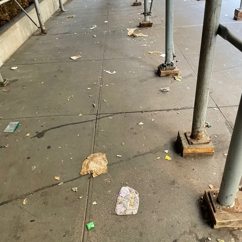 Litter scattered on the sidewalk beneath scaffolding.