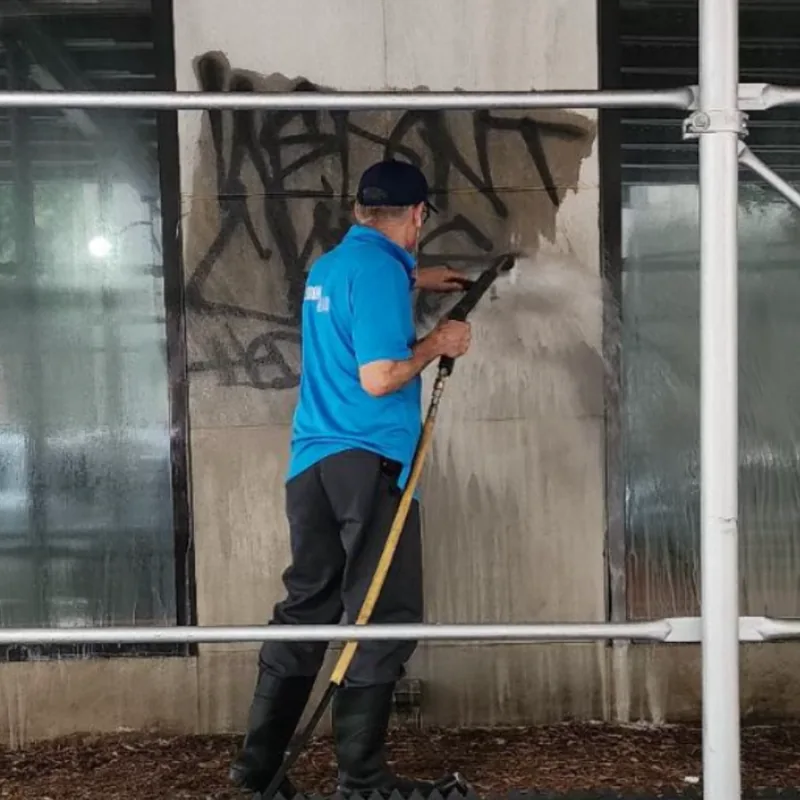 Graffiti being pressure-washed from a stone facade behind scaffolding.