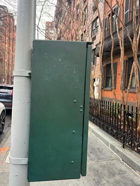 The green traffic control box with the dark graffiti painted over.