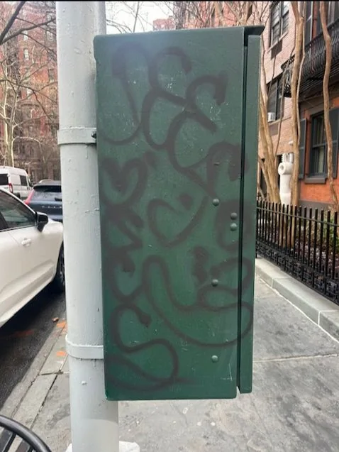 Dark graffiti on a green traffic control box beside a gray pole.