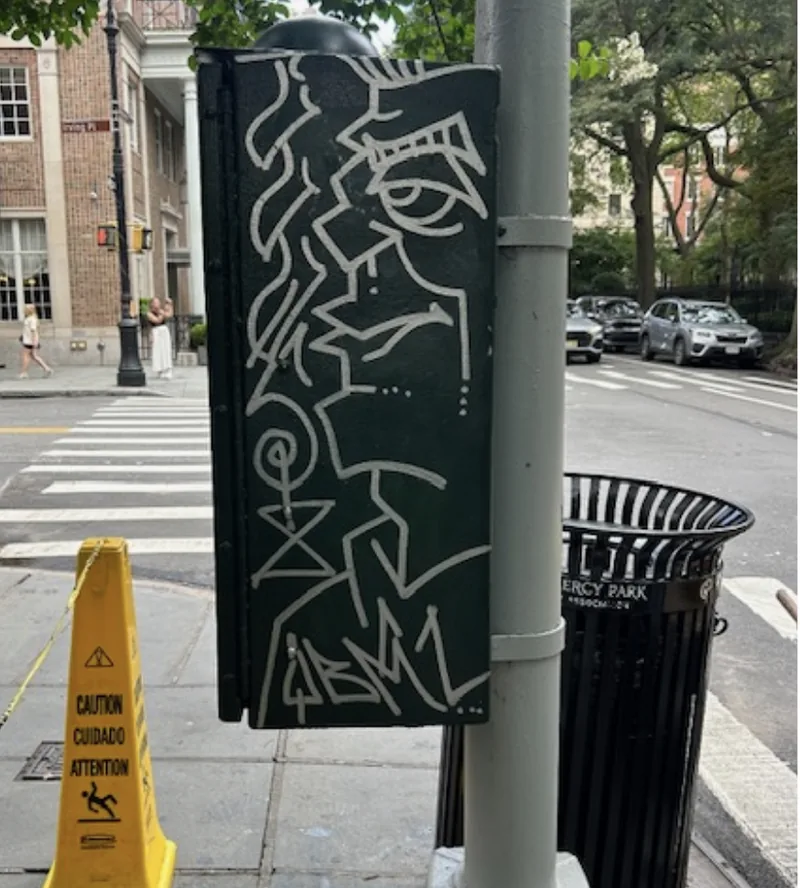 White graffiti on a green traffic control box beside a crosswalk.