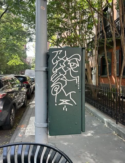 White graffiti on a green traffic control box beside a gray pole.