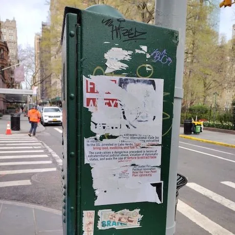 Posters and graffiti on the back of a green traffic control box.