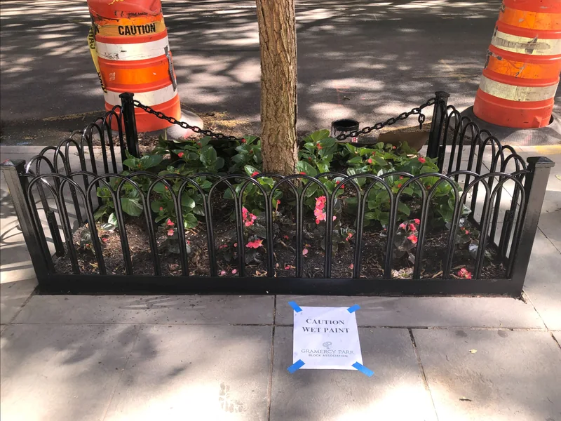The same tree garden fence after repainting, with a wet-paint sign.