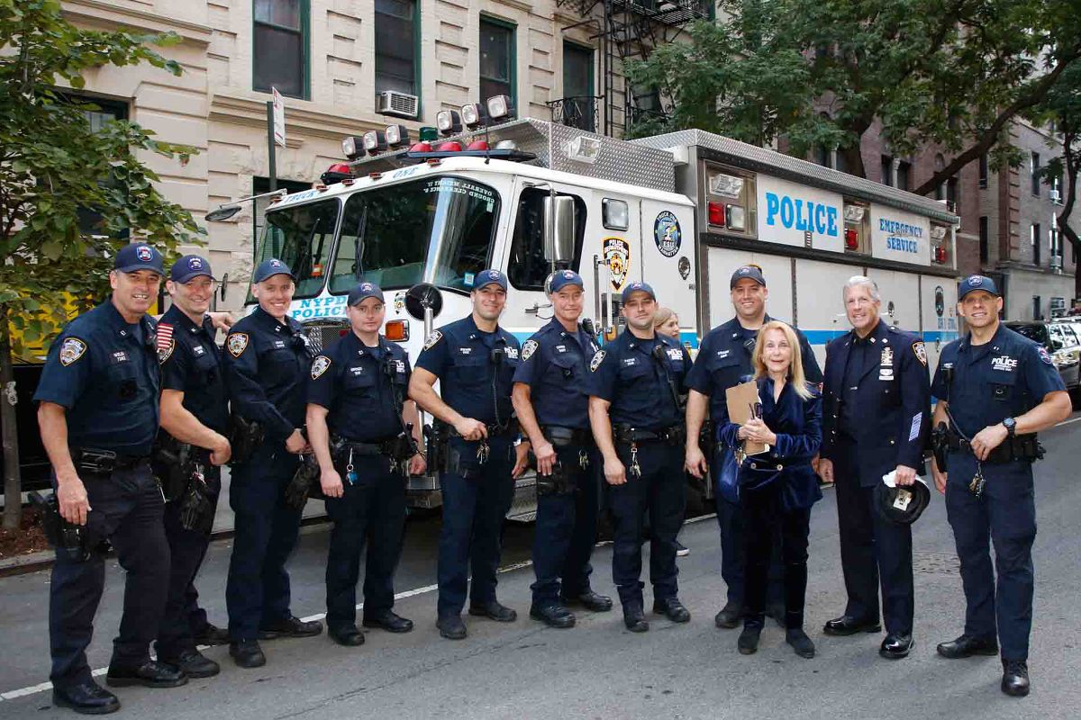 A neighborhood gathering with uniformed NYPD officers beside an Emergency Service truck.